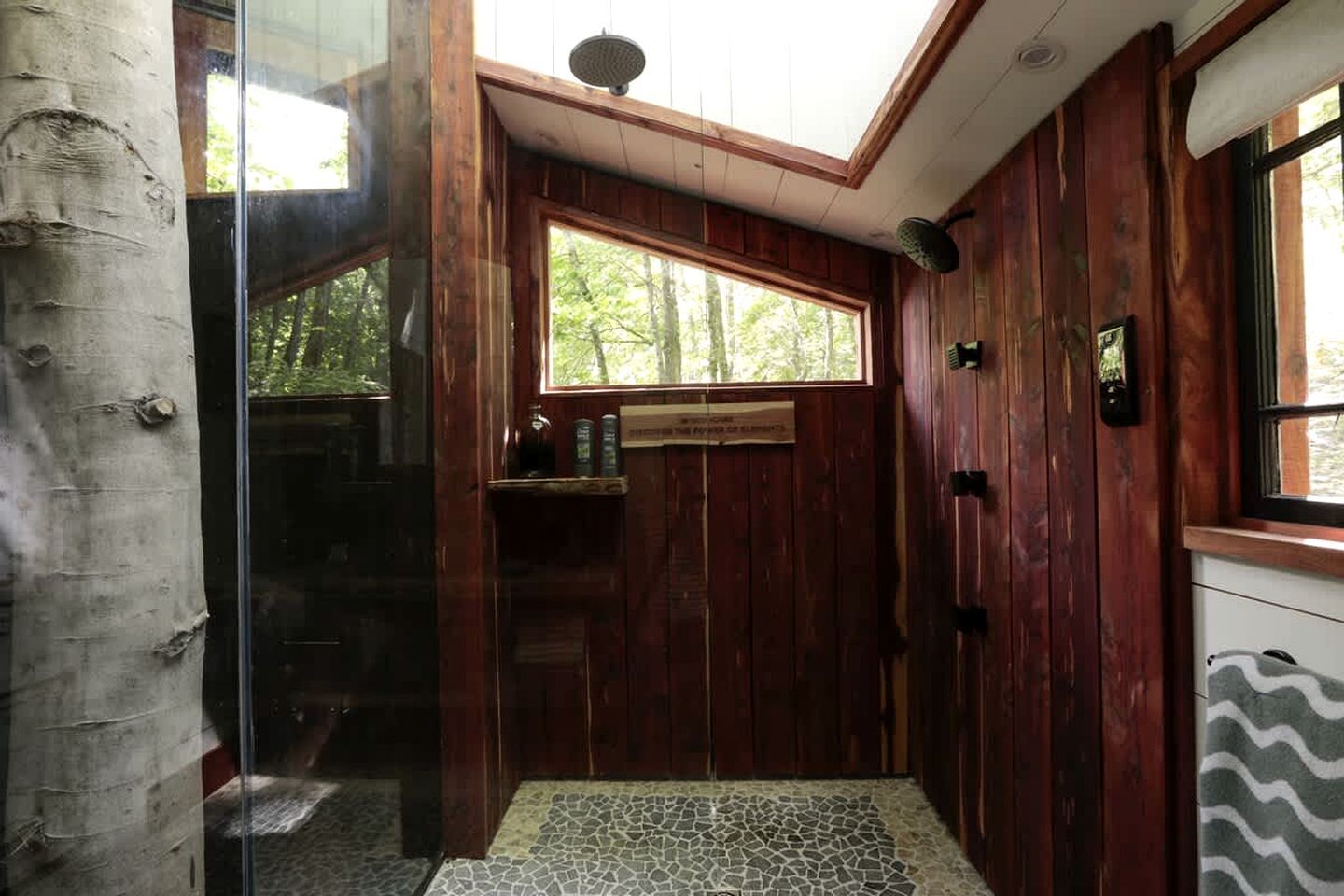 A wooden interior with a glass door leading outside, a window with a view of trees, and a tiled floor.