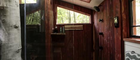 Un intérieur en bois avec une porte vitrée donnant sur l’extérieur, une fenêtre offrant une vue sur les arbres et un sol carrelé.