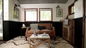 A room with a brown leather sofa, a wooden coffee table, a white rug, and wooden paneling on the walls. - Romantic Tree House near Chattanooga in the North Georgia Woodlands (Flintstone)
