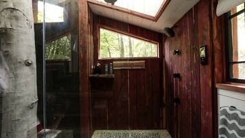 A wooden interior with a glass door leading outside, a window with a view of trees, and a tiled floor.