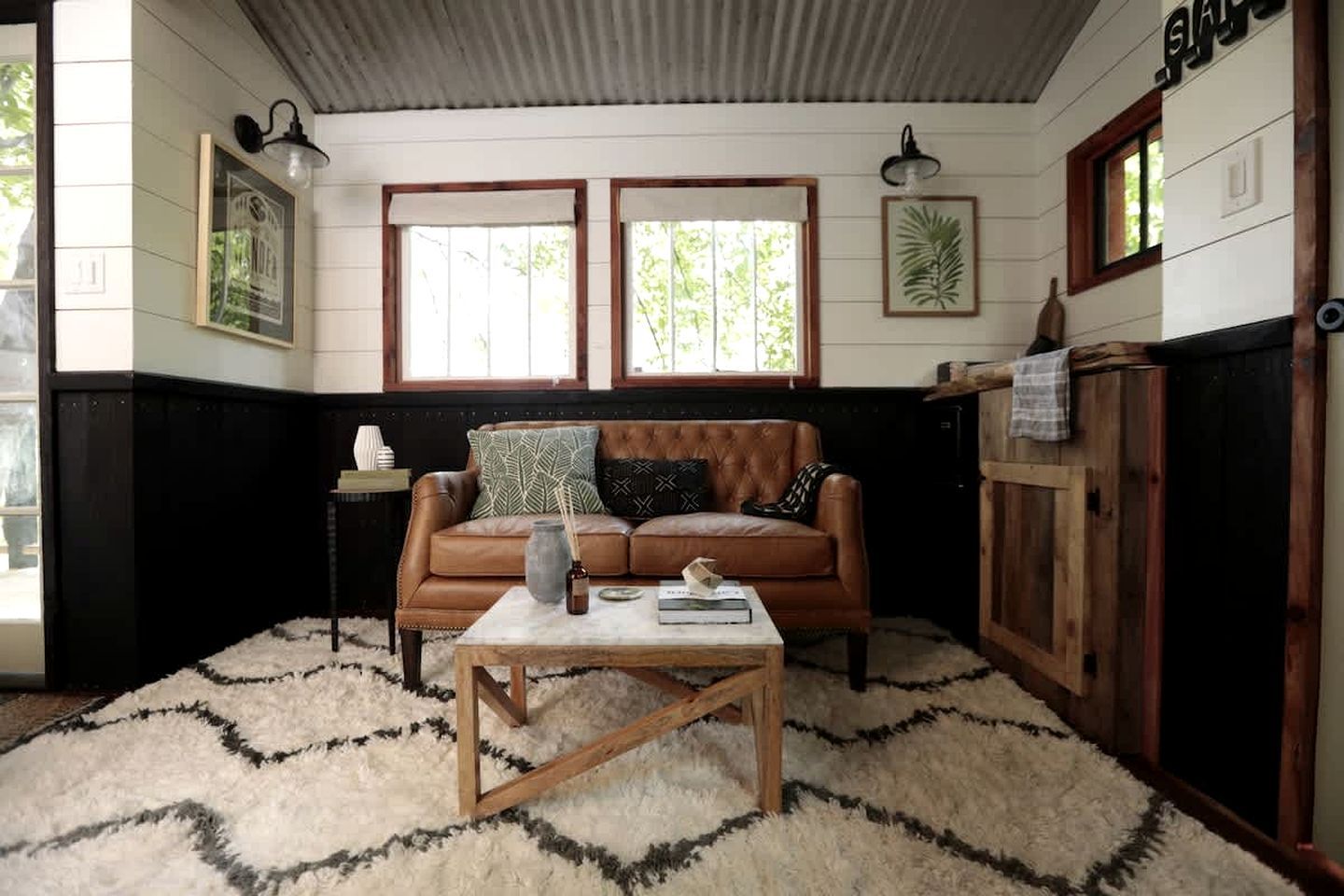 A room with a brown leather sofa, a wooden coffee table, a white rug, and wooden paneling on the walls.