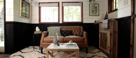 A room with a brown leather sofa, a wooden coffee table, a white rug, and wooden paneling on the walls.