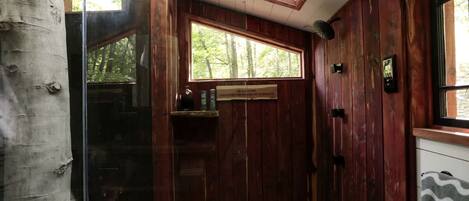 A wooden interior with a glass door leading outside, a window with a view of trees, and a tiled floor.