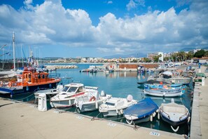A marina with various boats docked, a clear sky, and buildings in the background.