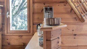 A wooden cabin interior with a window, a kettle, a bowl, and a digital camera on a counter.