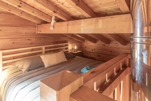 A wooden cabin interior with a bunk bed, a small table with a lamp, and a metal container.