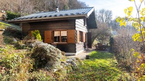 A wooden cabin with a sloped roof, a chimney, and a small porch with a table and chairs.