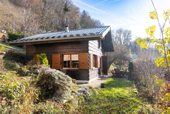 A wooden cabin with a sloped roof, a chimney, and a small porch with a table and chairs.