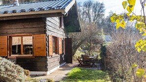 A wooden cabin with a covered patio, a chimney, and a view of the surrounding trees.