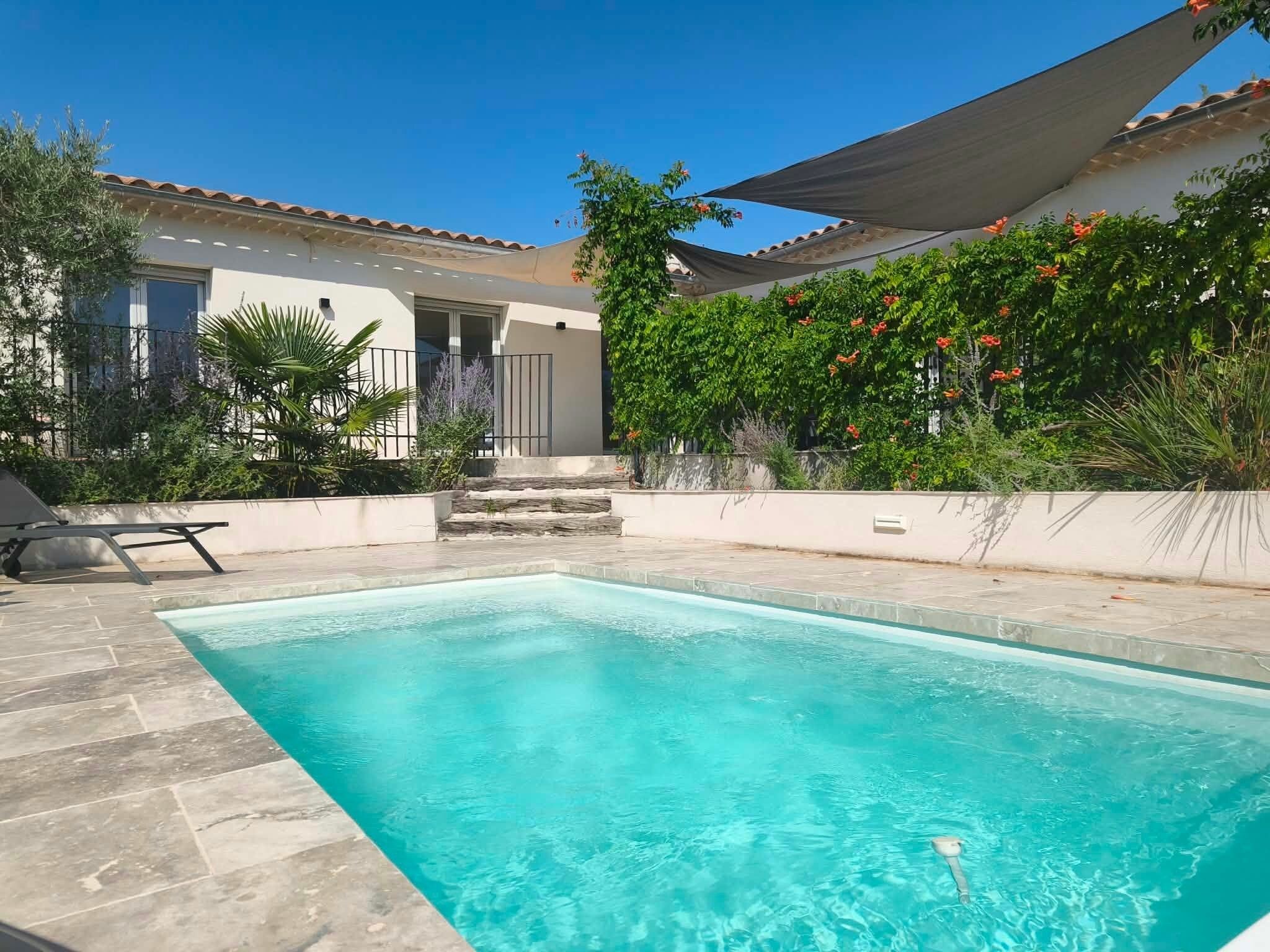 Una piscina rectangular con agua cristalina azul, rodeada por un solárium con baldosas.