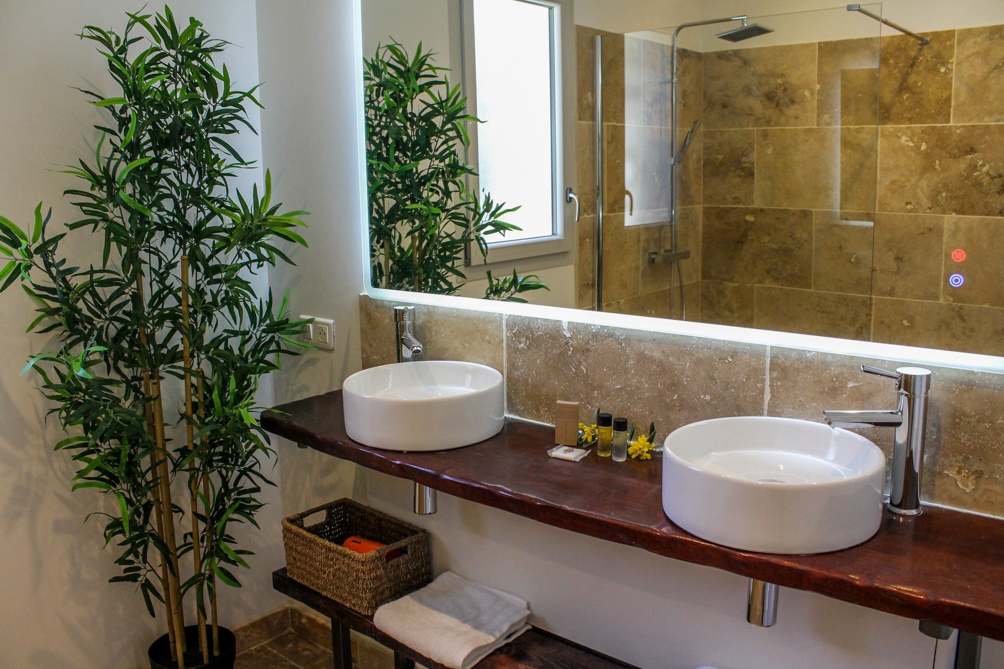 Une salle de bain avec deux lavabos, un grand miroir et une plante en bambou.