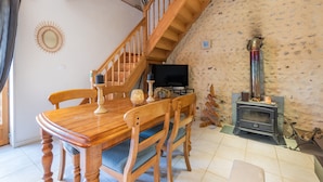 A dining area with a wooden table and chairs, a staircase, a television, and a stone wall. - Holiday Home “Galets” with Mountain View, Wi-Fi, and Air Conditioning (Peyraube)