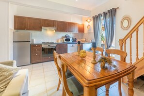 A kitchen with wooden cabinets, a refrigerator, stove, microwave, and a dining area with a wooden table and chairs. - Holiday Home 'Galets' with Mountain View, Wi-Fi and Air Conditioning (Peyraube)