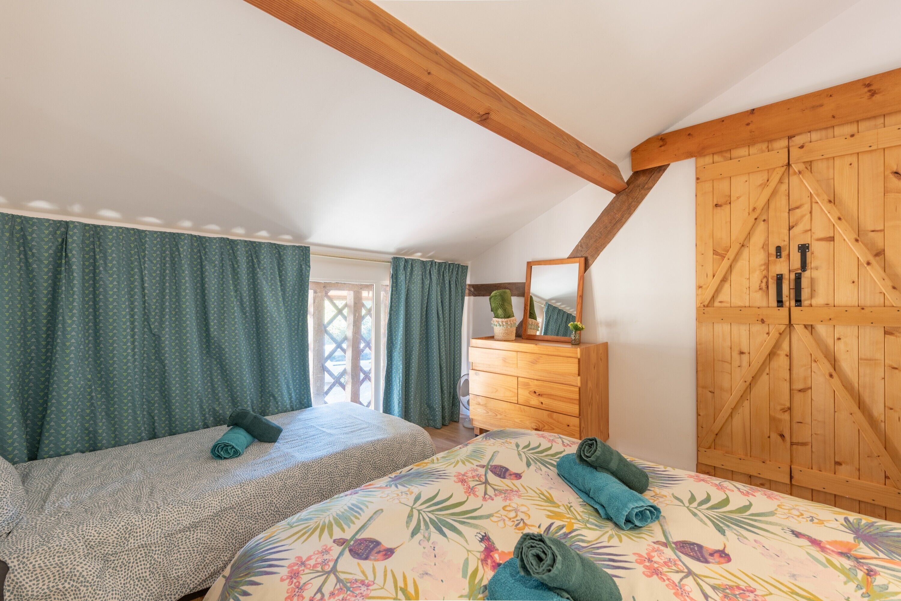 Un dormitorio con dos camas, un armario de madera, un espejo y una ventana con cortinas.