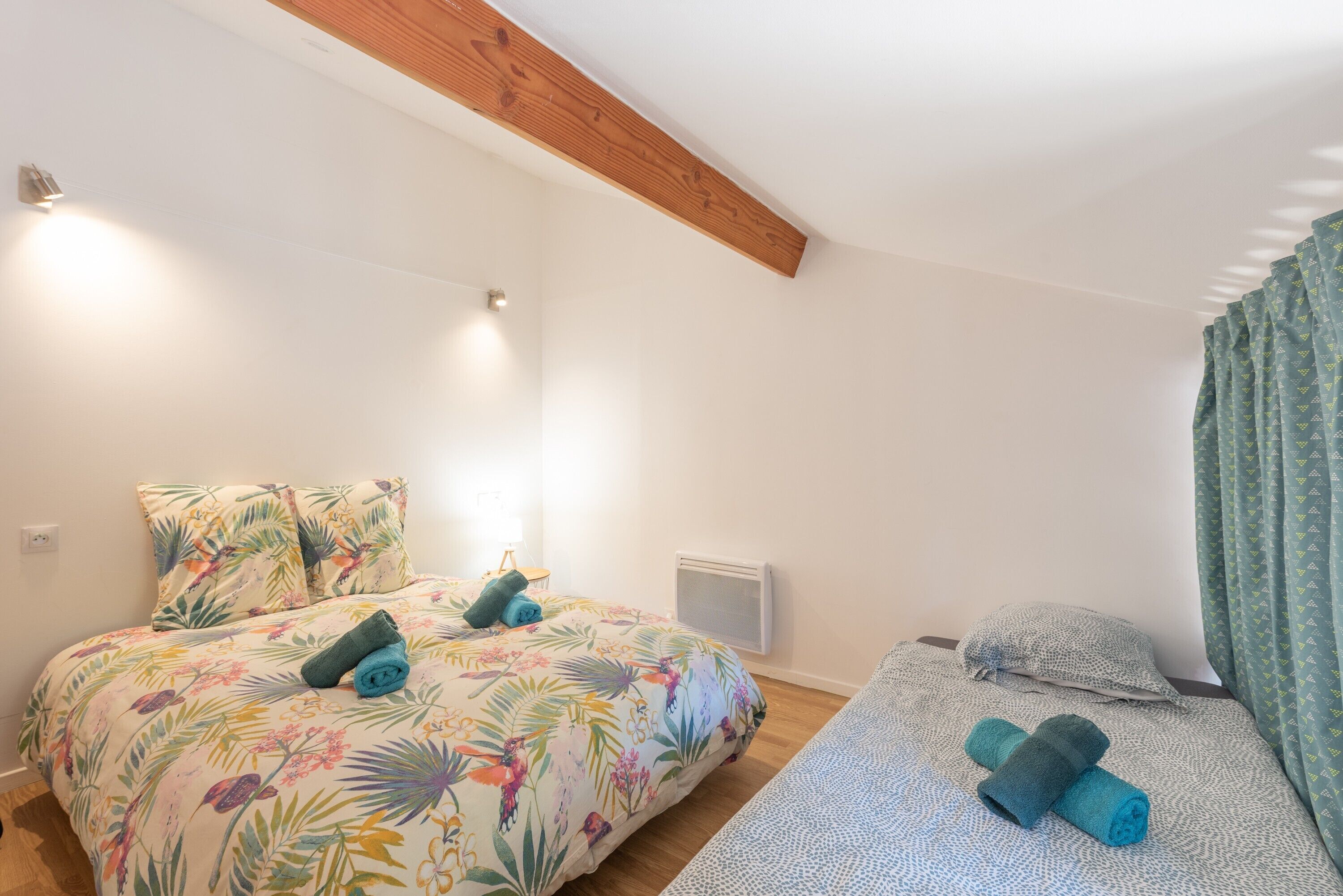 A bedroom with a bed, a smaller bed, a heater, and a window with curtains.