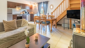 A living room with a sofa, a coffee table with a plant, a dining area with a table and chairs, a kitchen with cabinets and appliances, and a staircase. - Holiday Home “Galets” with Mountain View, Wi-Fi, and Air Conditioning (Peyraube)