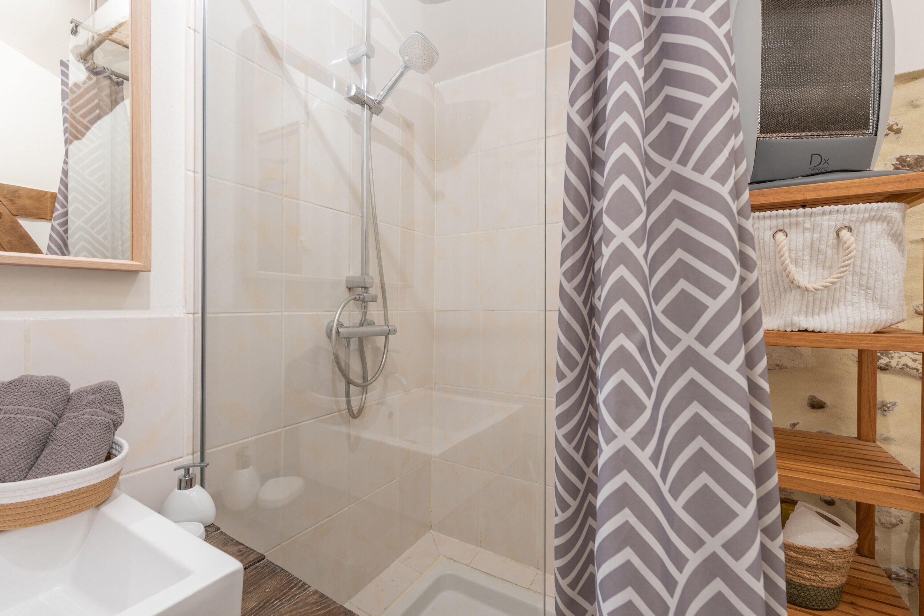 Une douche avec une porte en verre, un porte-serviettes et une étagère en bois avec des paniers.