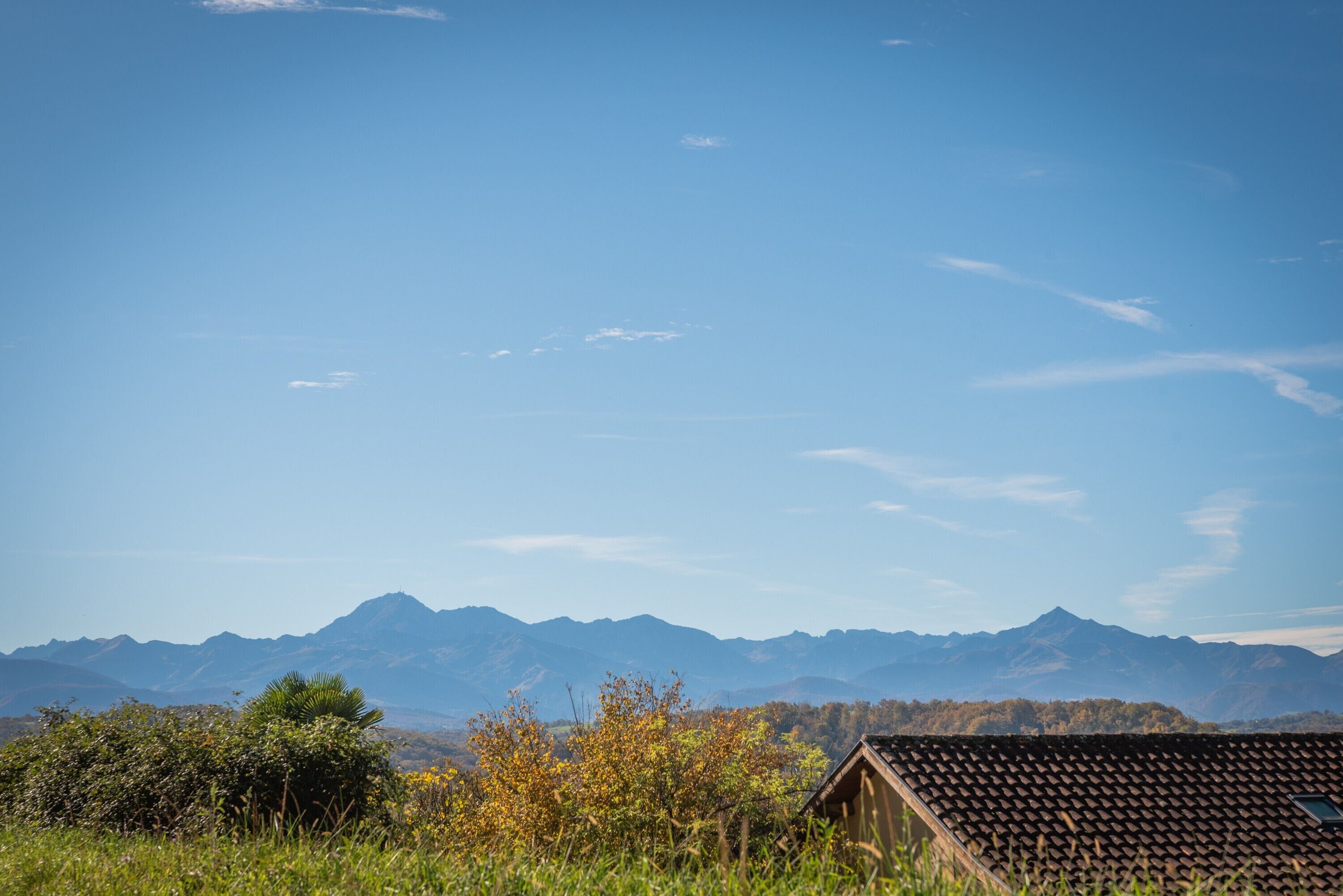 Eine gebirgige Landschaft mit blauem Himmel, ein Gebäude mit Ziegeldach und ein kleines Fenster.