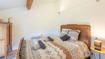 A bedroom with a wooden headboard, patterned bedding, a bedside table with a lamp, and a wooden wardrobe.