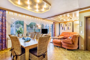 A room with a dining table, wicker chairs, a sofa, and a television.