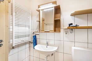 Ein Badezimmer mit einem weißen Waschbecken, einem Spiegel, einem Handtuchhalter und einem Fenster mit Jalousien.