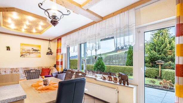 Ein modernes Wohnzimmer mit Essbereich, großen Fenstern und Blick auf den Garten.