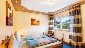 Ein Schlafzimmer mit Bett, Sessel, Fenster mit Vorhängen, Heizkörper und einem Bild an der Wand.
