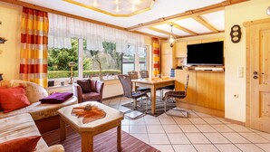 Ein gemütliches Wohnzimmer mit Sofa, Esstisch und Stühlen, einem Fernseher und einem Fenster mit Vorhängen.