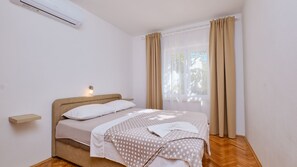Un dormitorio con cama, mesita de noche, aire acondicionado instalado en la pared y ventana con cortinas.