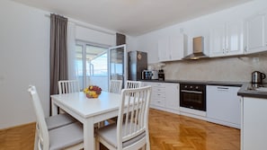A modern kitchen with white cabinets, a dining table with chairs, a refrigerator, a microwave, and a coffee maker.