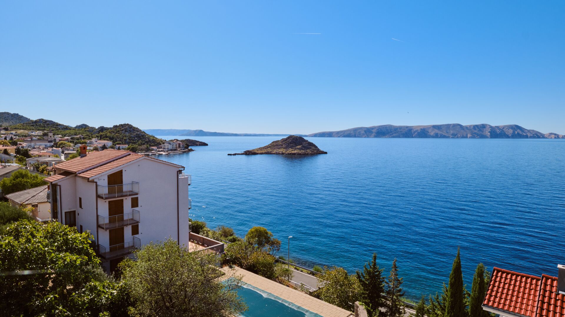 A coastal view with a building, a swimming pool, and a small island in the water.