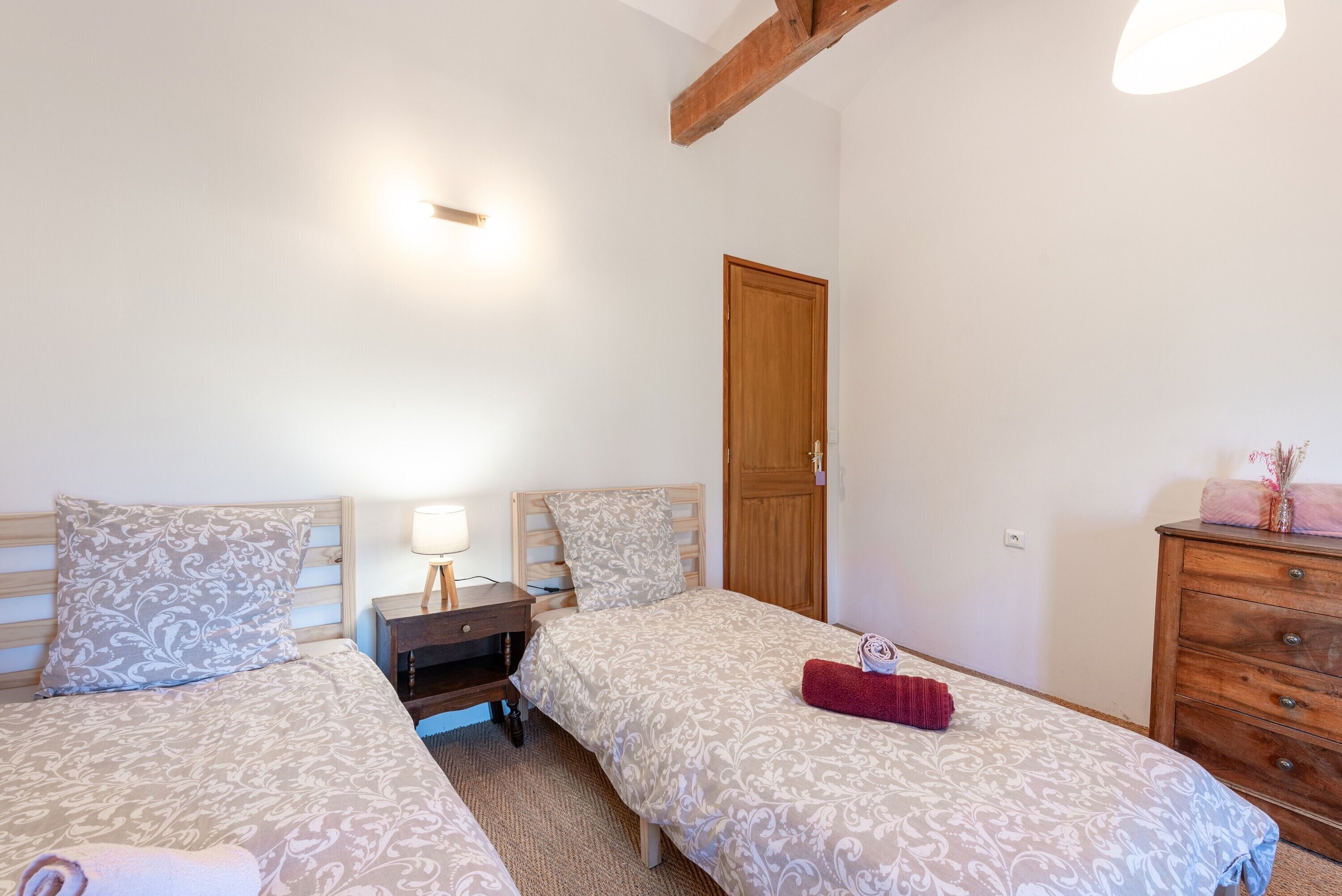 Une chambre avec deux lits, une commode en bois, une table de chevet et une porte.