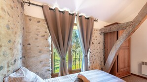 A bedroom with a stone wall, a bed with a rolled towel, and a wooden wardrobe. - Holiday Home “Tomettes” with Mountain View, Wi-Fi and Air Conditioning (Peyraube)
