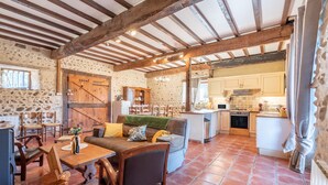 A rustic interior with a stone wall, wooden furniture, a kitchen area, and a dining space. - Holiday Home “Tomettes” with Mountain View, Wi-Fi and Air Conditioning (Peyraube)