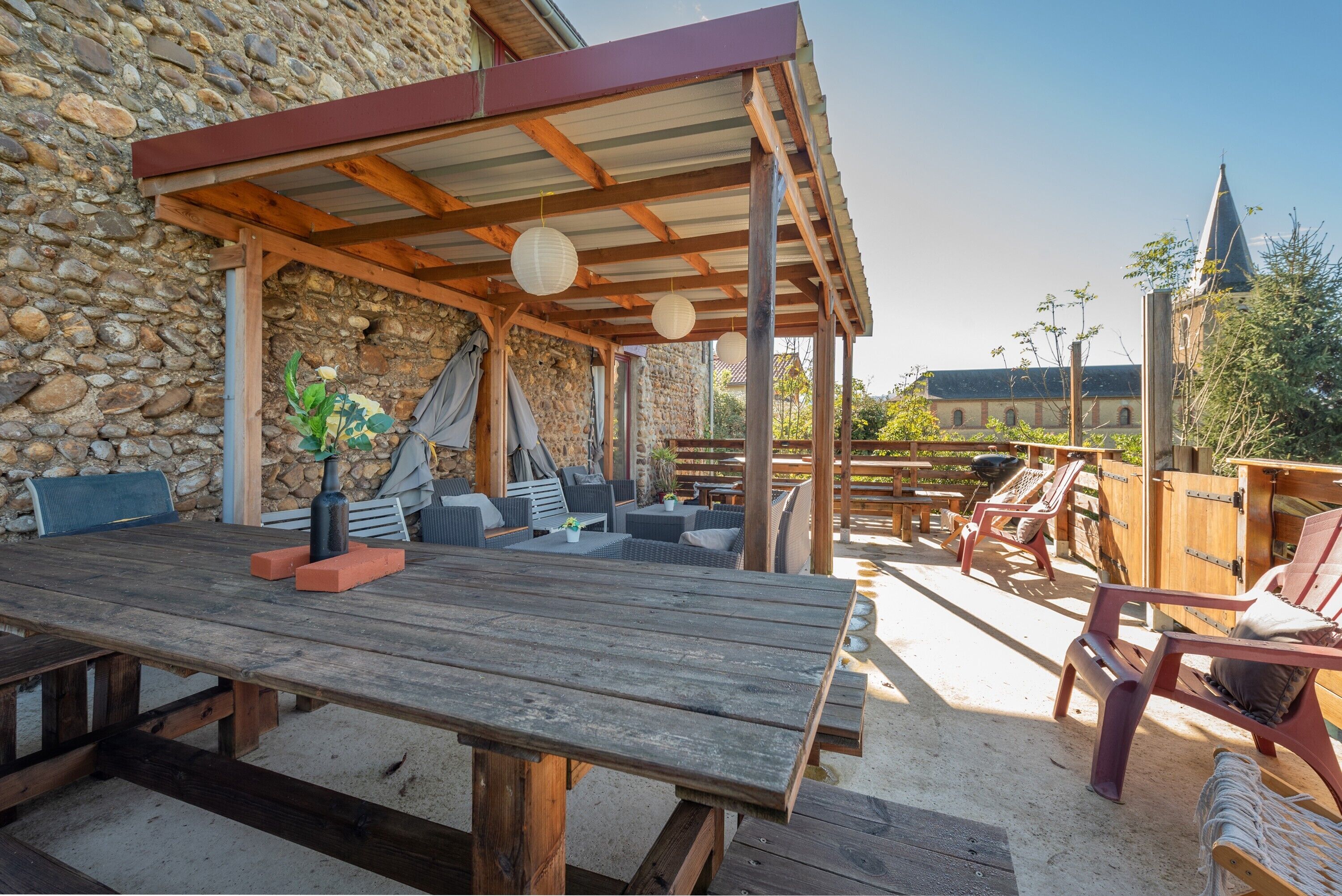 Een terras buiten met een houten tafel, stoelen en een stenen muur.