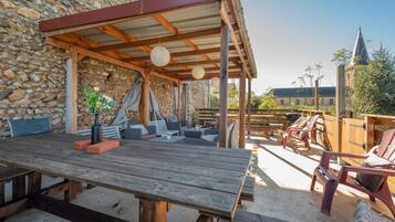 Een terras buiten met een houten tafel, stoelen en een stenen muur.
