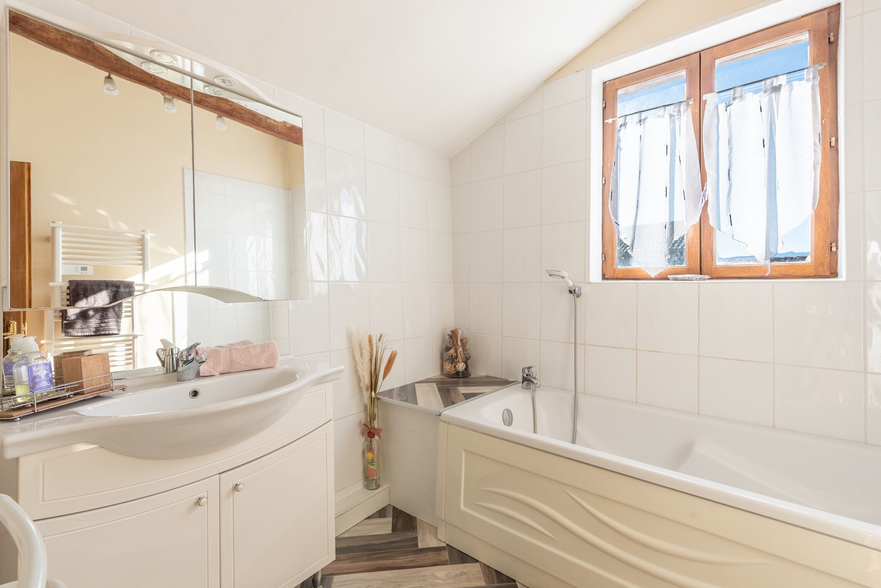 Un bany amb un lavabo gran, una banyera, una finestra amb cortines i un mirall.
