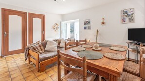 A dining area with a wooden table, chairs, and a television. - Gary Loup Holiday Home: Mountain View, Private Terrace, Wi-Fi (sazos)