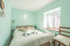 Un dormitorio con cama, mesita de noche, lámpara, ventana y una silla.