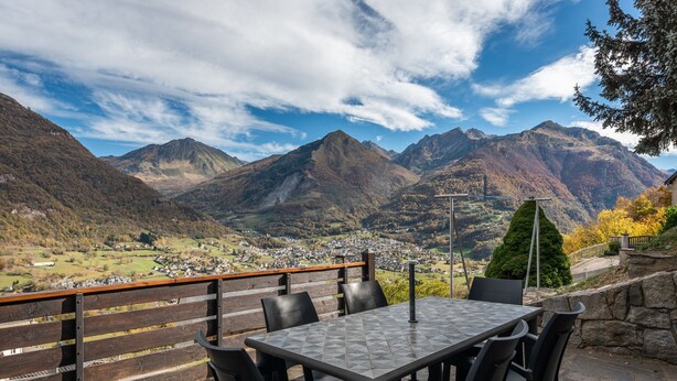 A table with chairs, a view of a valley, mountains, and a town.