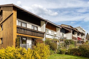 Una fila di case in legno tradizionali con balconi, un giardino e cielo sereno.