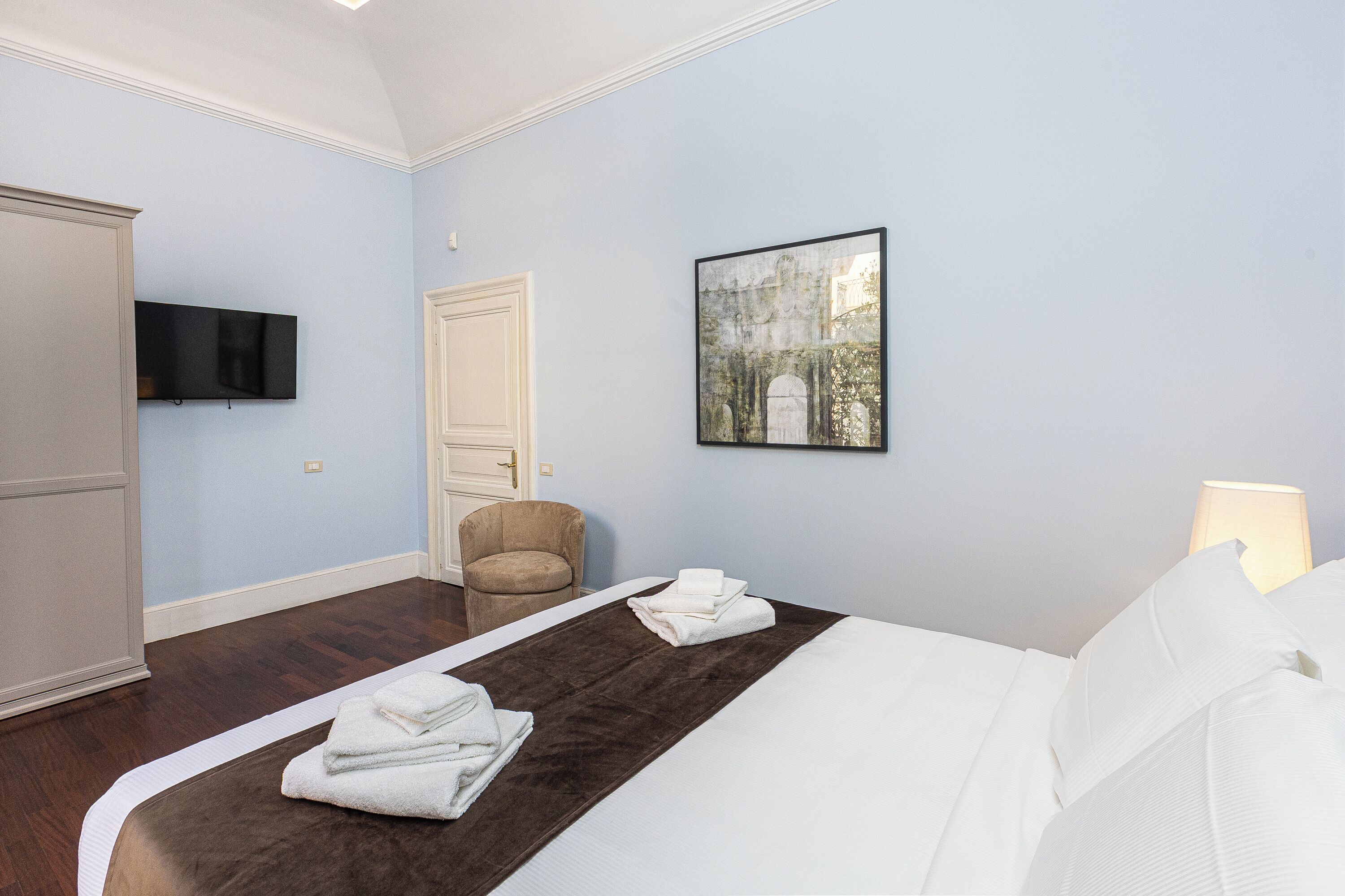 A bedroom with a bed, a chair, a television, and a painting on the wall.