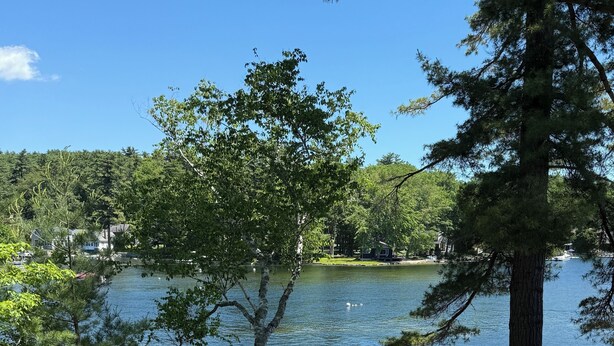 A lakeside deck with outdoor seating and a dock extending into the water. - Sebago Lake studio-style condo with enclosed sunroom and sunset views (Standish)