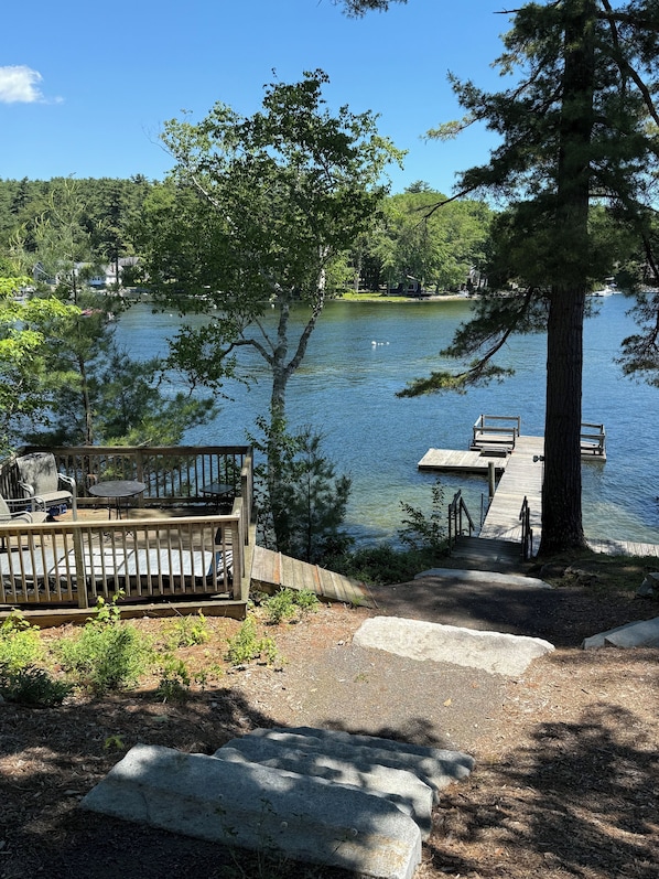 A lakeside deck with outdoor seating and a dock extending into the water.