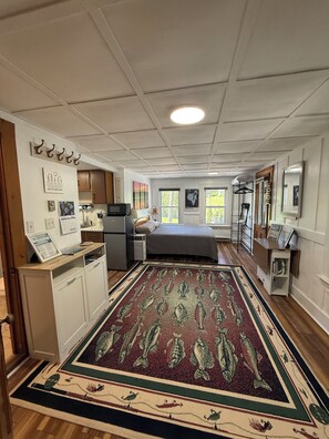 A bedroom with a bed, a desk, a dresser, a television, and a window with a view of trees. - Sebago Lake studio-style condo with enclosed sunroom and sunset views (Standish)