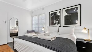 Un dormitorio moderno con cama, mesitas de noche, un espejo y obras de arte en la pared.