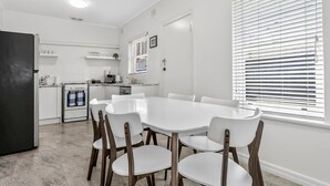 Una cocina moderna con armarios blancos, una mesa de comedor con sillas y una ventana con persianas.