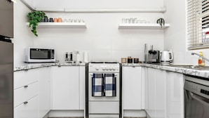 Una cocina compacta con gabinetes blancos, microondas, estufa y cafetera.