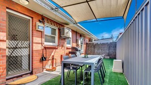 Un patio trasero con mesa, sillas, una parrilla y un área cubierta.