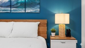 Une chambre à coucher avec une tête de lit en bois, un lit blanc, une table de chevet avec une lampe, une petite plante en pot et une paire de chaussons.